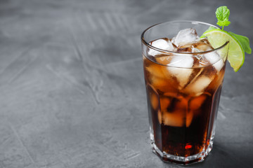 Glass of Rum and Cola cocktail on grey stone table, space for text