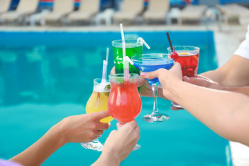 Friends clinking glasses with fresh summer cocktails near swimming pool, closeup