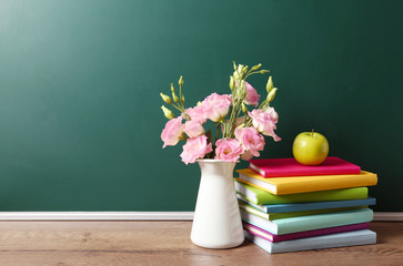 Vase of flowers, books and apple on wooden table near green chalkboard, space for text. Teacher's...