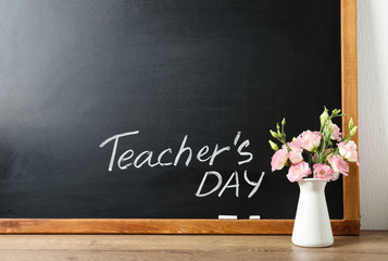 Fototapeta na wymiar Blackboard with inscription TEACHER'S DAY and vase of flowers on wooden table, space for text