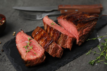Board with slices of grilled meat on grey table, closeup