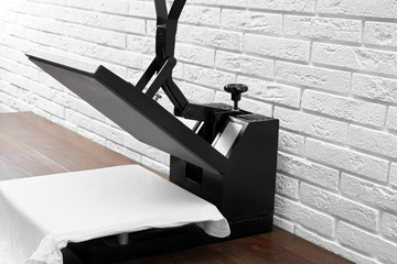 Heat press machine with t-shirt on wooden table near white brick wall