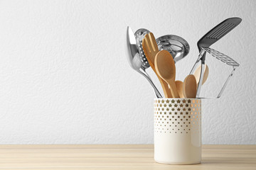 Set of kitchen utensils in stand on wooden table near light wall. Space for text