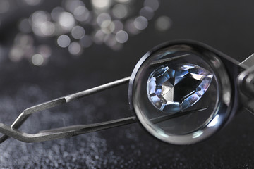 Tweezers with precious jewel over table, view through magnifier