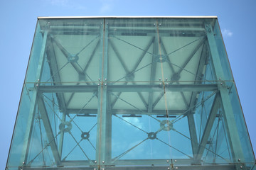 Fototapeta premium modern glass tower structure with visible metal framework inside. The building stands against a clear blue sky, highlighting its transparent and architectural design.