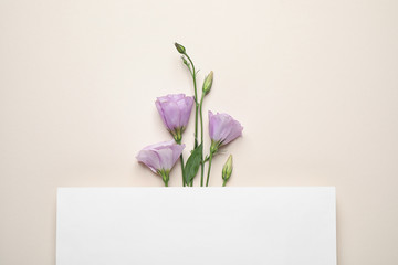 Flat lay composition with beautiful Eustoma flowers and card on beige background, space for text