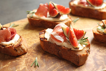 Bruschettas with cream cheese, prosciutto and figs served on wooden board, closeup