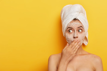 Surprised young girl removes dead cells and bacteria from face with peeling natural sea salt mask,...