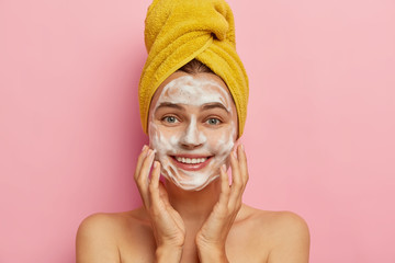 Face wash and hygiene concept. Young cheerful European woman cleans face with soap, touches cheeks...