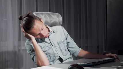 Young man falling asleep late at night sitting in front of the computer. Male freelancer looking tired, falling asleep while working on his project online. Work, overworking concept