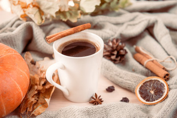  mug of hot black coffee with cinnamon stick on the background of gray sweater, yellow dry fallen leaves, red pumpkin, autumn
