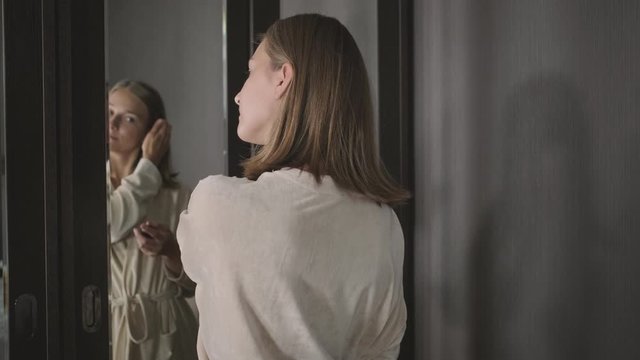 Woman is looking at mirror and correcting her hairstyle