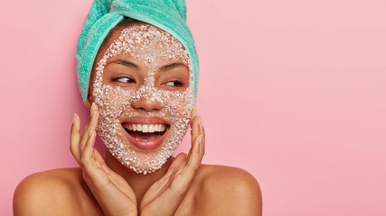 Portrait of happy cheerful woman improves condition of face skin, applies peeling mask, wants to...