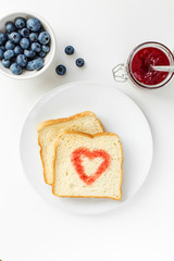 Breakfast with toast heart of berry jam on the white table, top view