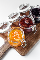 three open jars with different jam on a wooden board