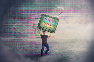 Angry gamer lifting up and throwing his old TV box after glitch text game over on the screen. Addicted, guy playing video games, lost in virtual reality world. Modern entertainment technology.
