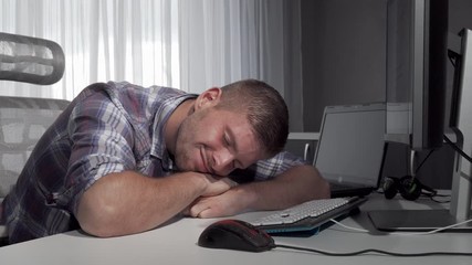 Man sleeping on his desk after finishing working on the computer. Young it industry worker resting after working on a project online. Male freelancer sleeping in front of a computer