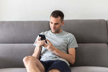 man at home sitting on couch reading phone message.