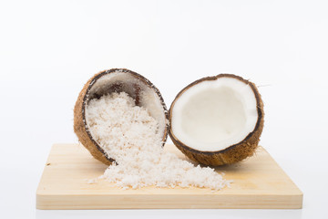 Coconut shell and grated coconut flakes on a brown wooden board isolated on white background.