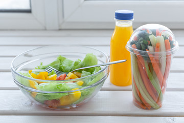Bowl of green salad, raw vegetables and bottle of orange juice. Weight loss, diet and right nutrition concept
