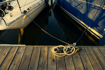 Naklejka premium Two sailboats parking at the wooden dock on the water with ropes tied on the pier