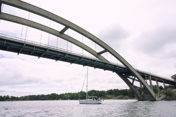 Sailboat passing under the big bridge on the sea in Sweden with white clouds sky