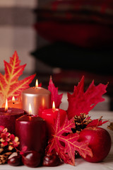 Autumn still life - candles, leaves and cones on the background of pillows.