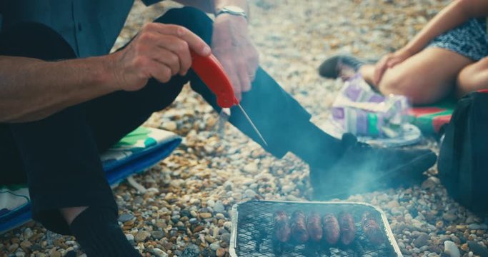 Senior mam using meat thermometer at beach barbecue