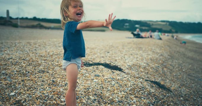 Happy little toddler on the beach throwing stones