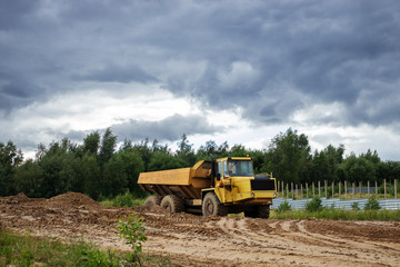 Obraz premium construction site with dump, truck, tree, cloudy sky