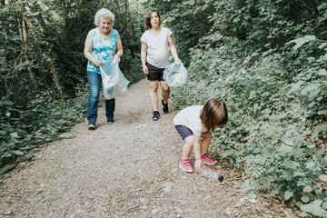 girl collecting plastic in the field, with her mother and grandmother