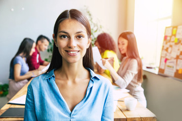 Attractive confident modern business woman in casual clothes looks at the camera and smiling. Modern start-up business team. Co-workers or students 