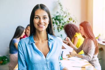 Attractive confident modern business woman in casual clothes looks at the camera and smiling. Modern start-up business team. Co-workers or students 