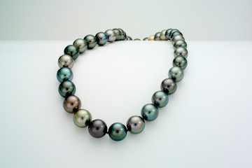 A necklace of a single strand of Tahitian pearls is laid over a curve white surface.