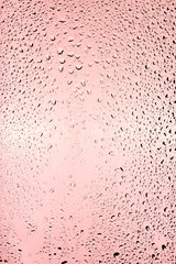 Drops of water flow down a transparent glass on a pink background.	
