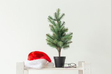 celebration, winter holidays and advertisement concept - small christmas tree and santa hat over white background
