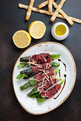 Rolls with carpaccio beef and salad leaves, flatlay on a dark brown metal background, vertical shot