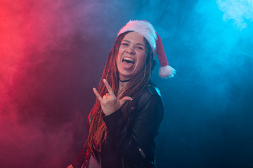 Rock, christmas and holidays concept - emotional woman in santa hat shows tongue and rock