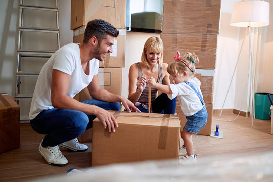 Happy Parents With Child Moving In New Home Unpacking Boxes.