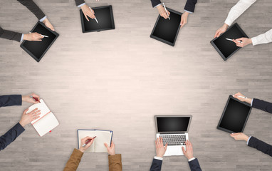 Group of people with devices in hands having desk discussion and making reports together on laptop,...