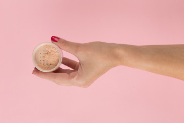 Fototapeta premium Girl hand holds powder from on a pink background. Makeup artist concept, copy space.