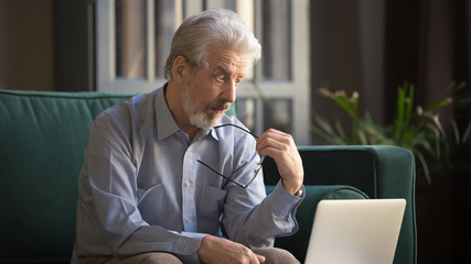 Pensive mature man distracted from computer thinking
