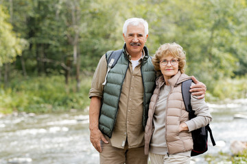 Happy mature male hiker embracing his wife by forest river during trip