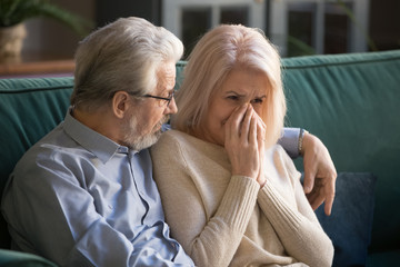 Elder mature husband supporting gray-haired wife at home.