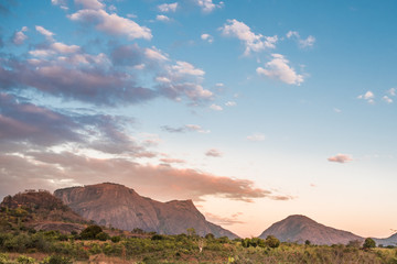 Fototapeta na wymiar Mountain range and fields in rural Mozambique under a blue sky with pink and purple clouds from the setting sun. Nampula Province, Mozambique, Africa