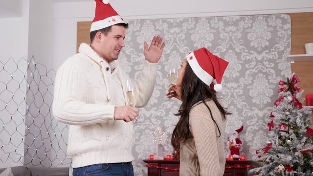 Happy smiling couple holding champagne glass in hands dancing and having fun in Christmas decorated room, slow motion close up shot