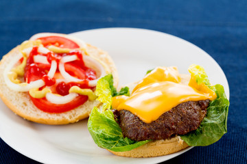 Hamburger with melted cheese on top and vegetables on the side on a plate