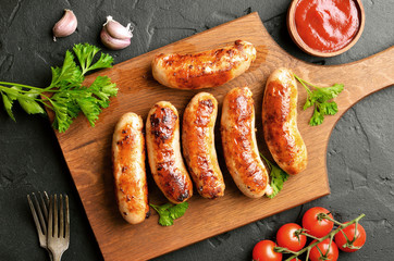 Roasted sausages on a cutting board, sause and cherry tomatoes