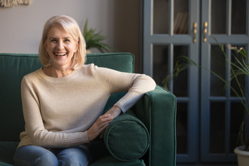 Happy senior woman of 60s sitting on couch at home