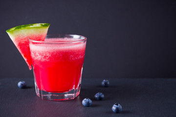 Watermelon drink in glasses with slices of watermelon. Watermelon smoothies and blueberries on dark background. Summer healthy drink for vegetarian. Copy space